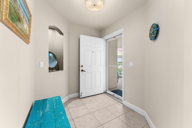 doorway featuring light tile patterned flooring, a textured ceiling, and baseboards