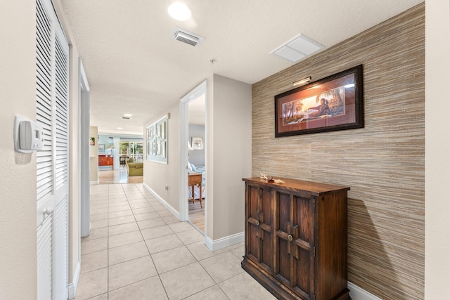 hall with an accent wall, light tile patterned flooring, visible vents, and baseboards