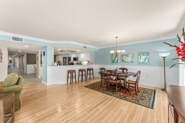 dining room with visible vents, light wood-style flooring, an inviting chandelier, wainscoting, and a textured ceiling