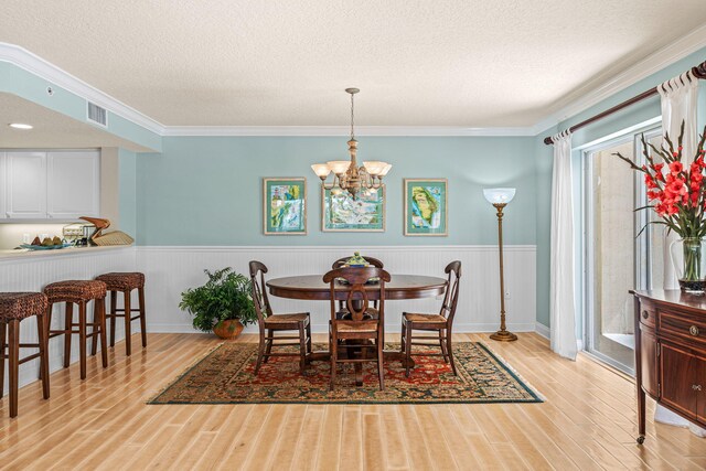 dining space featuring a textured ceiling, a notable chandelier, a wainscoted wall, wood finished floors, and visible vents