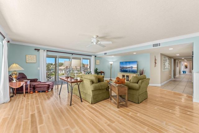 living area with light wood finished floors, visible vents, a textured ceiling, and ornamental molding