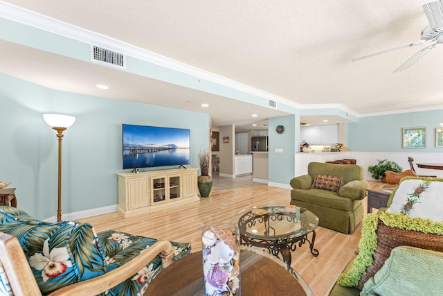 living area with visible vents, baseboards, a ceiling fan, light wood-style flooring, and crown molding