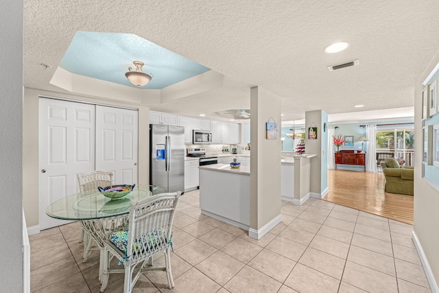 kitchen with visible vents, white cabinets, a raised ceiling, stainless steel appliances, and light tile patterned flooring