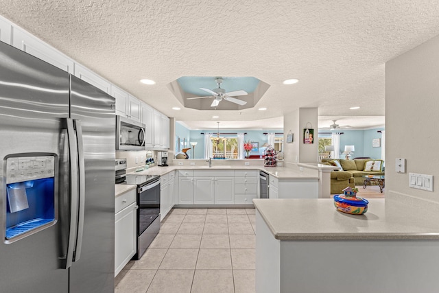 kitchen featuring light tile patterned floors, stainless steel appliances, a raised ceiling, white cabinetry, and a peninsula