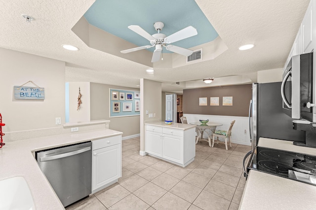 kitchen with white cabinets, a raised ceiling, a wainscoted wall, appliances with stainless steel finishes, and light countertops