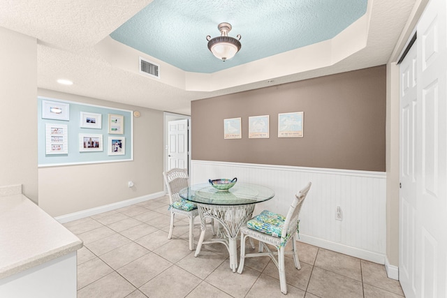 dining space with a textured ceiling, tile patterned flooring, a wainscoted wall, visible vents, and a tray ceiling