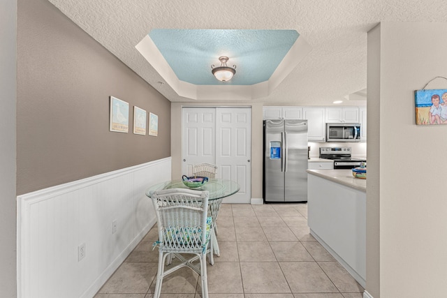 dining area with a wainscoted wall, a tray ceiling, a textured ceiling, and light tile patterned flooring