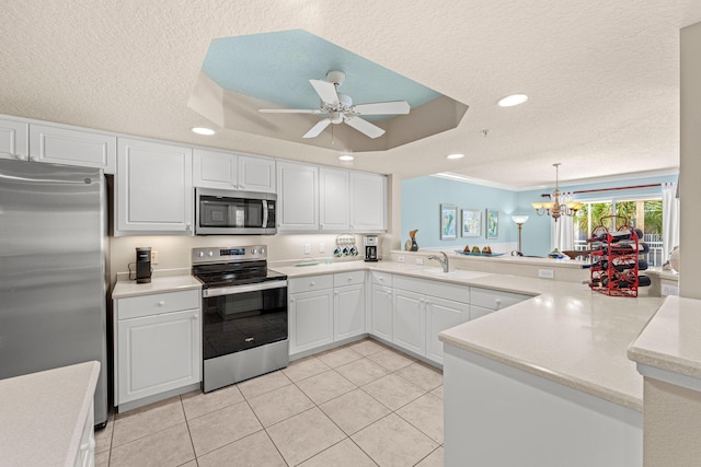 kitchen featuring a textured ceiling, a peninsula, light countertops, appliances with stainless steel finishes, and a raised ceiling