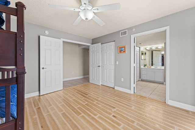 unfurnished bedroom featuring a textured ceiling, light wood-style flooring, a sink, visible vents, and a closet