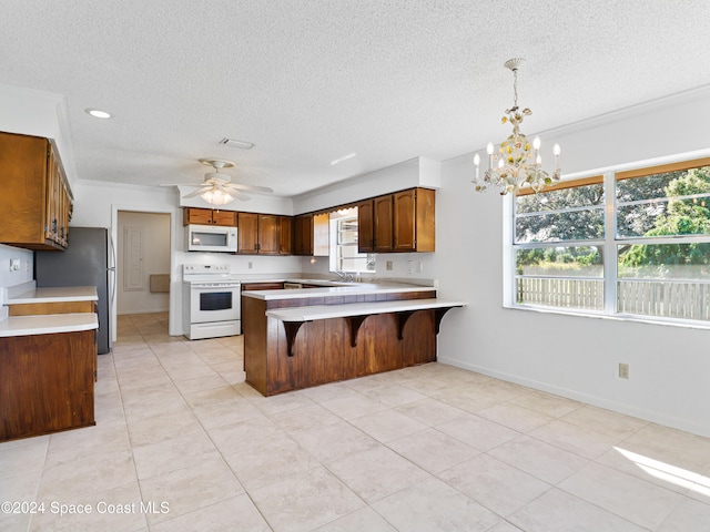 kitchen with kitchen peninsula, a textured ceiling, decorative light fixtures, white appliances, and ceiling fan with notable chandelier