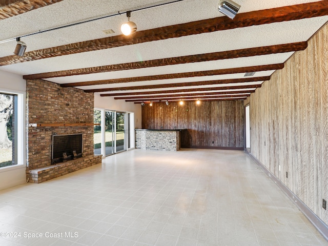 unfurnished living room featuring wood walls, rail lighting, a fireplace, a textured ceiling, and beamed ceiling