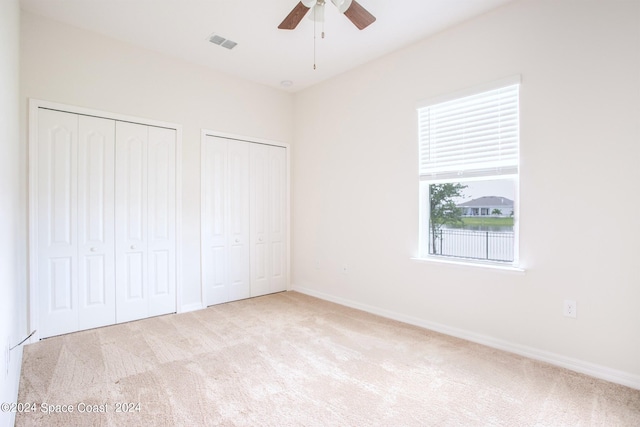 unfurnished bedroom featuring light carpet, ceiling fan, and two closets