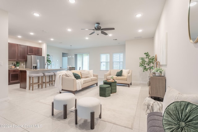 tiled living room with ceiling fan with notable chandelier and sink