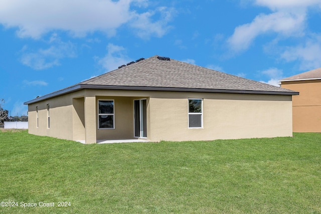 rear view of house featuring a shingled roof, a yard, and stucco siding