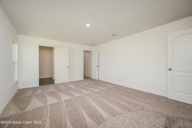 unfurnished bedroom featuring light carpet, a textured ceiling, visible vents, and baseboards