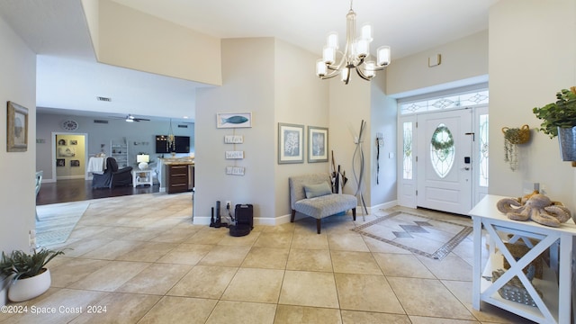 entrance foyer with visible vents, ceiling fan with notable chandelier, a high ceiling, light tile patterned floors, and baseboards