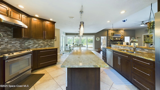 kitchen with a kitchen island, a sink, under cabinet range hood, appliances with stainless steel finishes, and tasteful backsplash