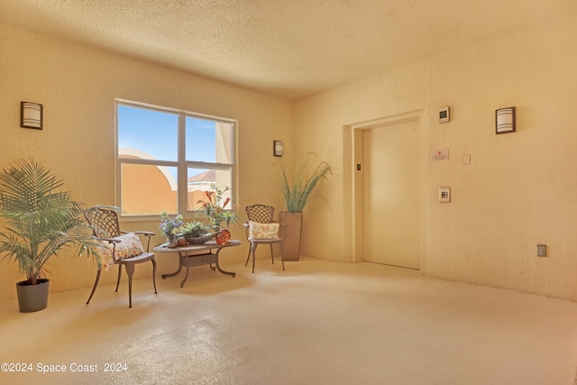 living area with a textured ceiling, elevator, and concrete flooring