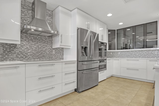 kitchen with light tile patterned floors, appliances with stainless steel finishes, white cabinetry, wall chimney exhaust hood, and tasteful backsplash