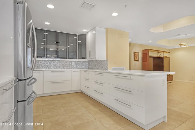 kitchen with white cabinets, backsplash, light tile patterned floors, stainless steel fridge, and kitchen peninsula