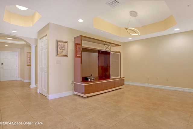 interior space featuring a tray ceiling, light tile patterned floors, and decorative columns