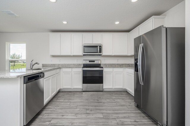 kitchen with kitchen peninsula, stainless steel appliances, sink, white cabinets, and light stone counters