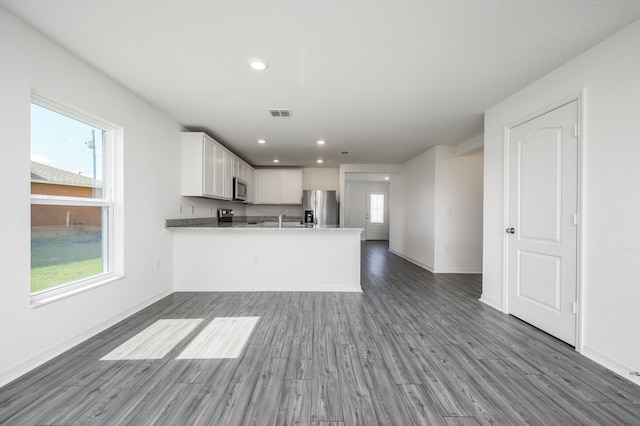 kitchen with a peninsula, stainless steel appliances, wood finished floors, white cabinetry, and light stone countertops