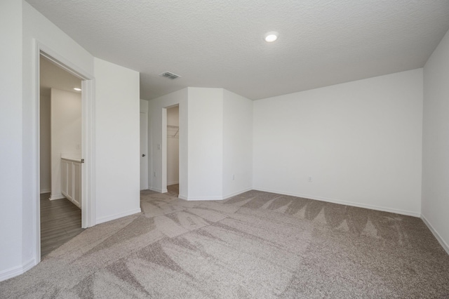 spare room with baseboards, visible vents, a textured ceiling, and light colored carpet