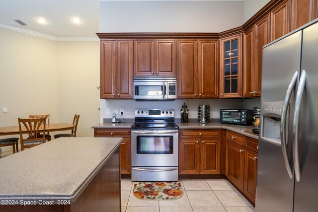 kitchen with appliances with stainless steel finishes, light tile patterned floors, a center island, and ornamental molding