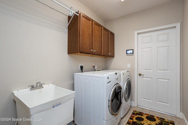 laundry area featuring light tile patterned floors, independent washer and dryer, sink, cabinets, and a textured ceiling