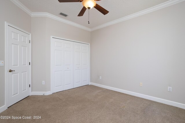 unfurnished bedroom with a textured ceiling, carpet flooring, a closet, ceiling fan, and ornamental molding