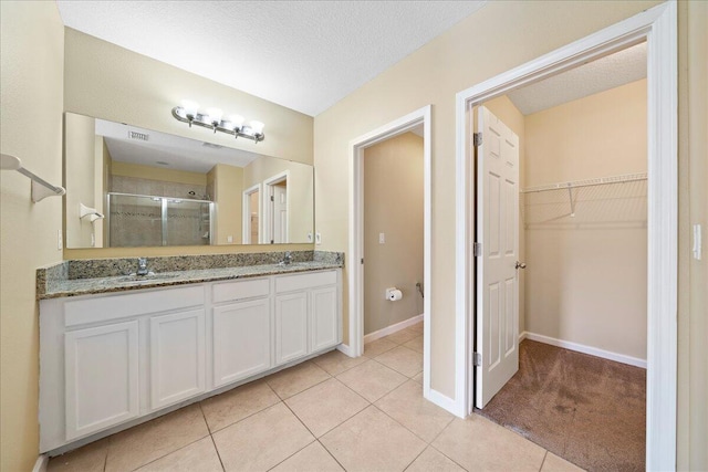 bathroom with double vanity, a sink, a shower stall, a spacious closet, and tile patterned floors