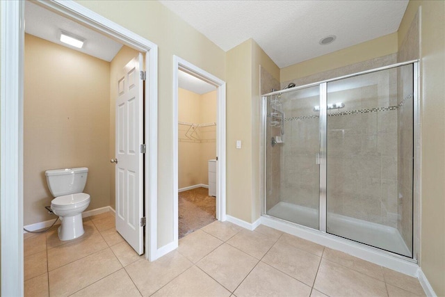 bathroom with a walk in closet, toilet, a shower stall, tile patterned flooring, and baseboards