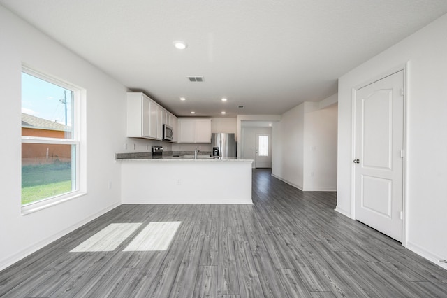 kitchen with appliances with stainless steel finishes, kitchen peninsula, white cabinets, and a healthy amount of sunlight