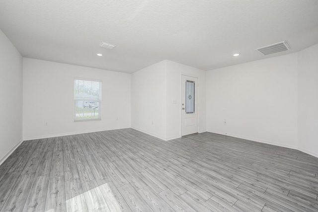 empty room with light wood-style floors, visible vents, and baseboards