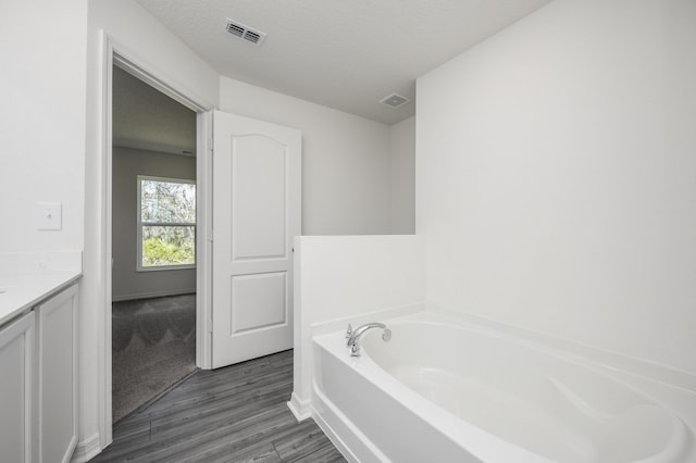 bathroom with visible vents, a textured ceiling, vanity, and a bath