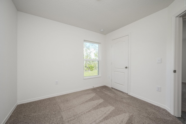 empty room featuring a textured ceiling, carpet flooring, and baseboards