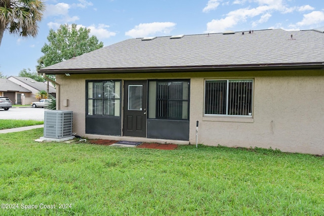 rear view of property with central air condition unit, a shingled roof, a lawn, and stucco siding