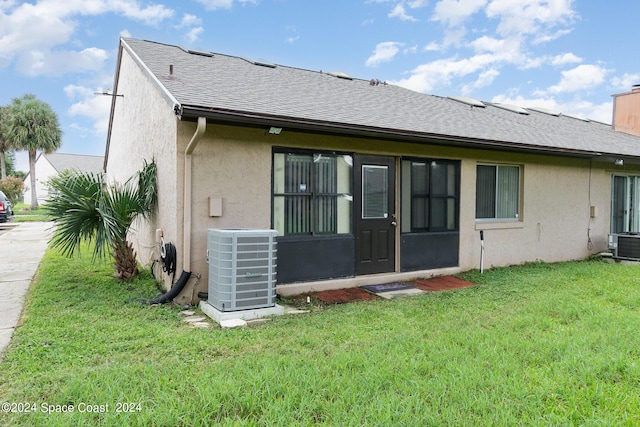 back of house with central air condition unit, a shingled roof, a lawn, and stucco siding