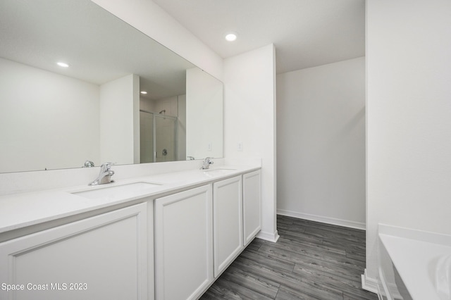 full bath featuring a shower stall, double vanity, wood finished floors, baseboards, and recessed lighting