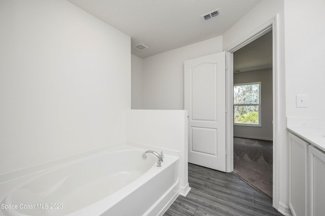 bathroom with a bath, wood finished floors, vanity, and baseboards