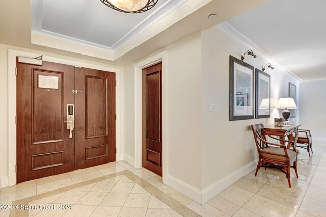 tiled foyer with a tray ceiling and crown molding