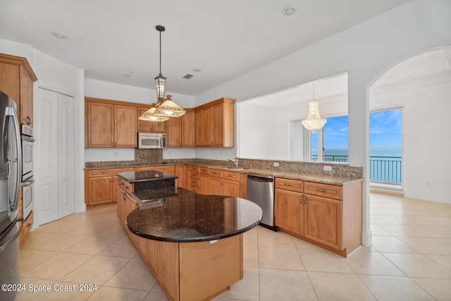 kitchen with a sink, a center island, dark stone counters, appliances with stainless steel finishes, and light tile patterned floors