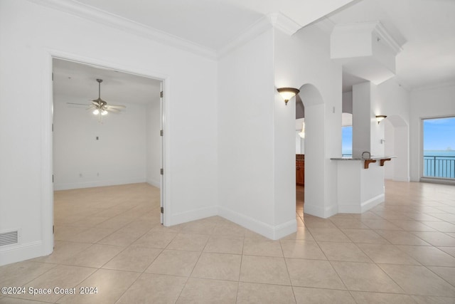 unfurnished room with light tile patterned floors, baseboards, arched walkways, ornamental molding, and ceiling fan