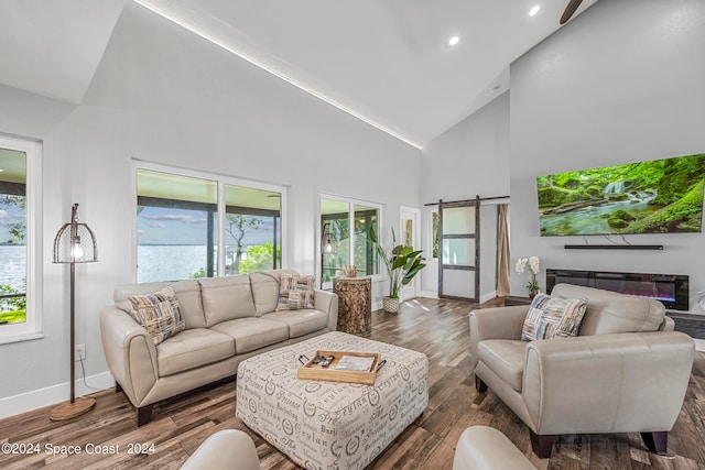 living room with high vaulted ceiling, a barn door, and dark hardwood / wood-style floors