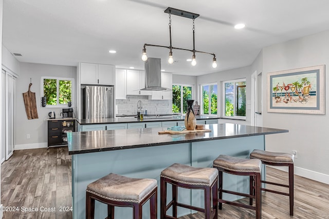 kitchen with a kitchen breakfast bar, stainless steel fridge, wood-type flooring, island range hood, and white cabinets