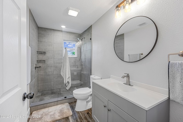 bathroom featuring hardwood / wood-style flooring, toilet, a tile shower, vanity, and a textured ceiling