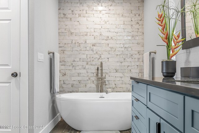 bathroom featuring a bath, hardwood / wood-style flooring, brick wall, and vanity