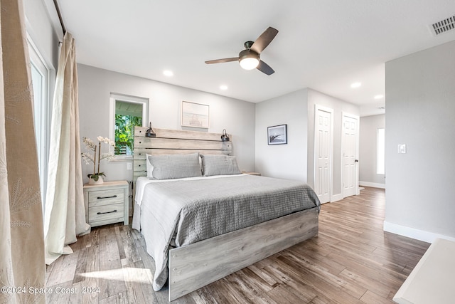 bedroom with ceiling fan, multiple closets, and light hardwood / wood-style flooring