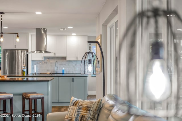 kitchen featuring white cabinets, wall chimney range hood, stainless steel fridge, decorative backsplash, and a breakfast bar